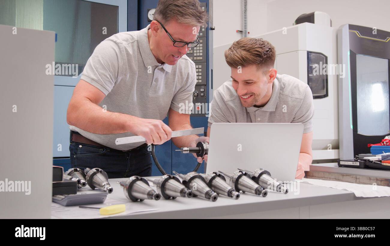 Male Engineer And Apprentice Measuring Components Whilst Looking At Laptop Stock Photo