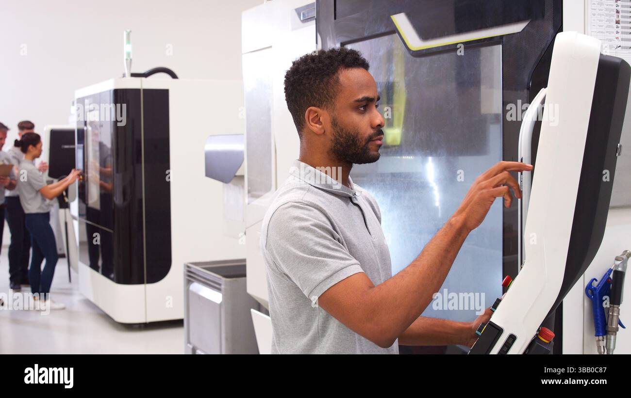 Male Engineer Or Apprentice Using CNC Machine In Factory Stock Photo