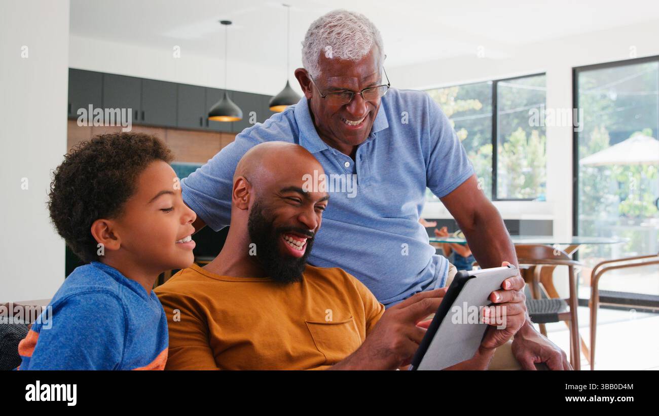 African American Family With Son Sitting On Sofa At Home Using Digital Tablet Stock Photo