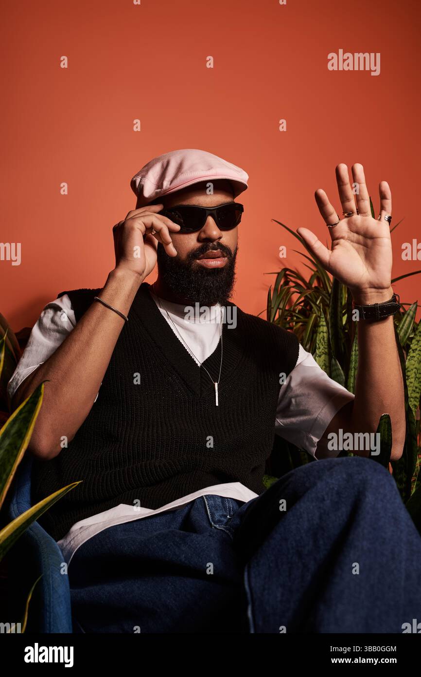 A fashionable young man wearing sunglasses and a cap enjoys a relaxed moment surrounded by greenery. Stock Photo