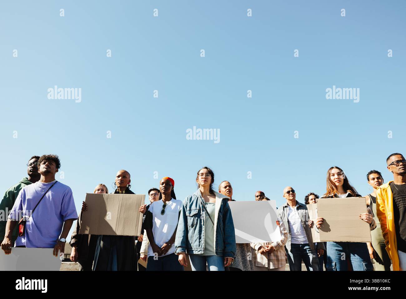A diverse group of people holding signs and gathering during a peaceful outdoor protest under a clear blue sky, expressing unity and belief in their c Stock Photo