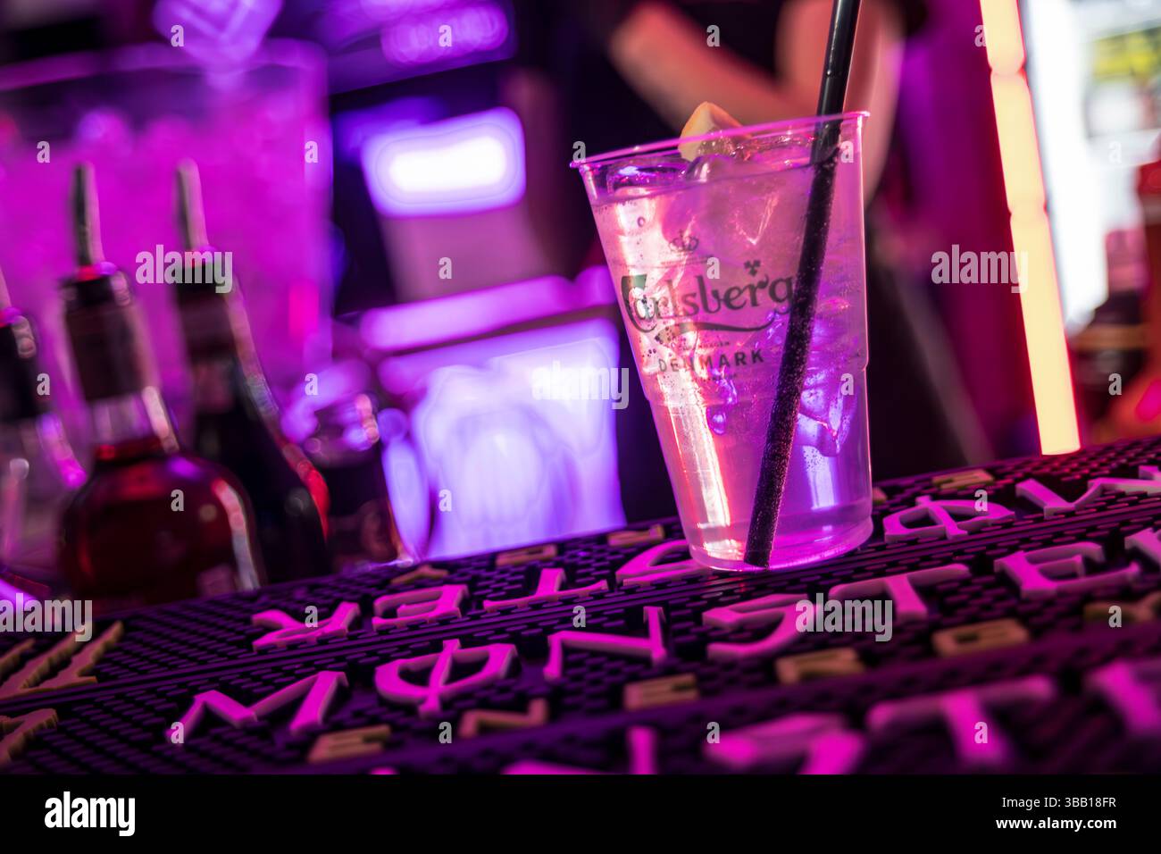 Rome, italy 4 may 2025: plastic cup with carlsberg beer, ice, lemon and  black straw on bar mat in purple-lit nightclub Stock Photo - Alamy, image size:1300x956