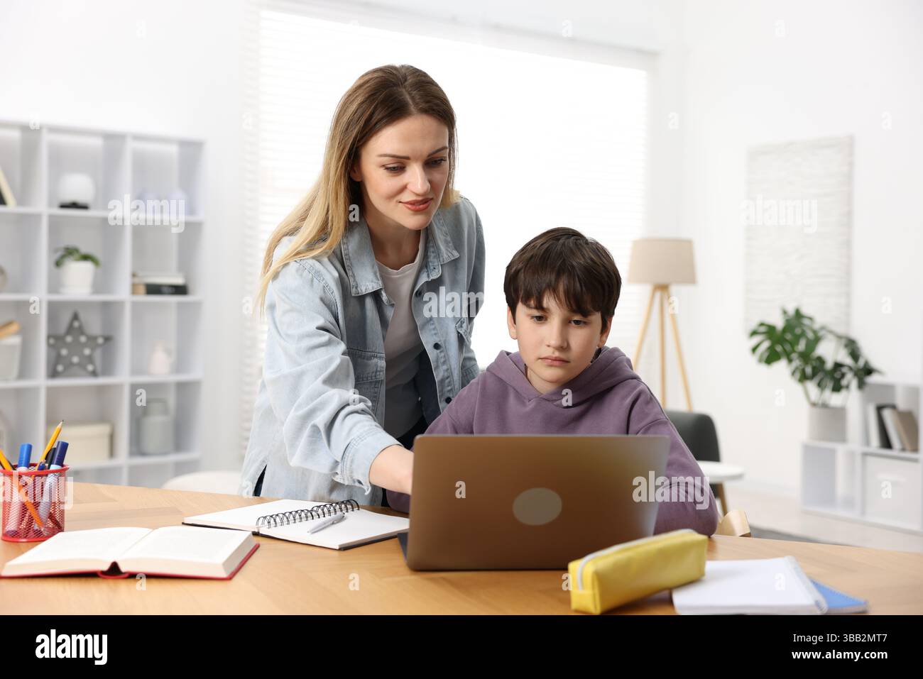 Mother helping her son with homework at wooden table indoors Stock ...