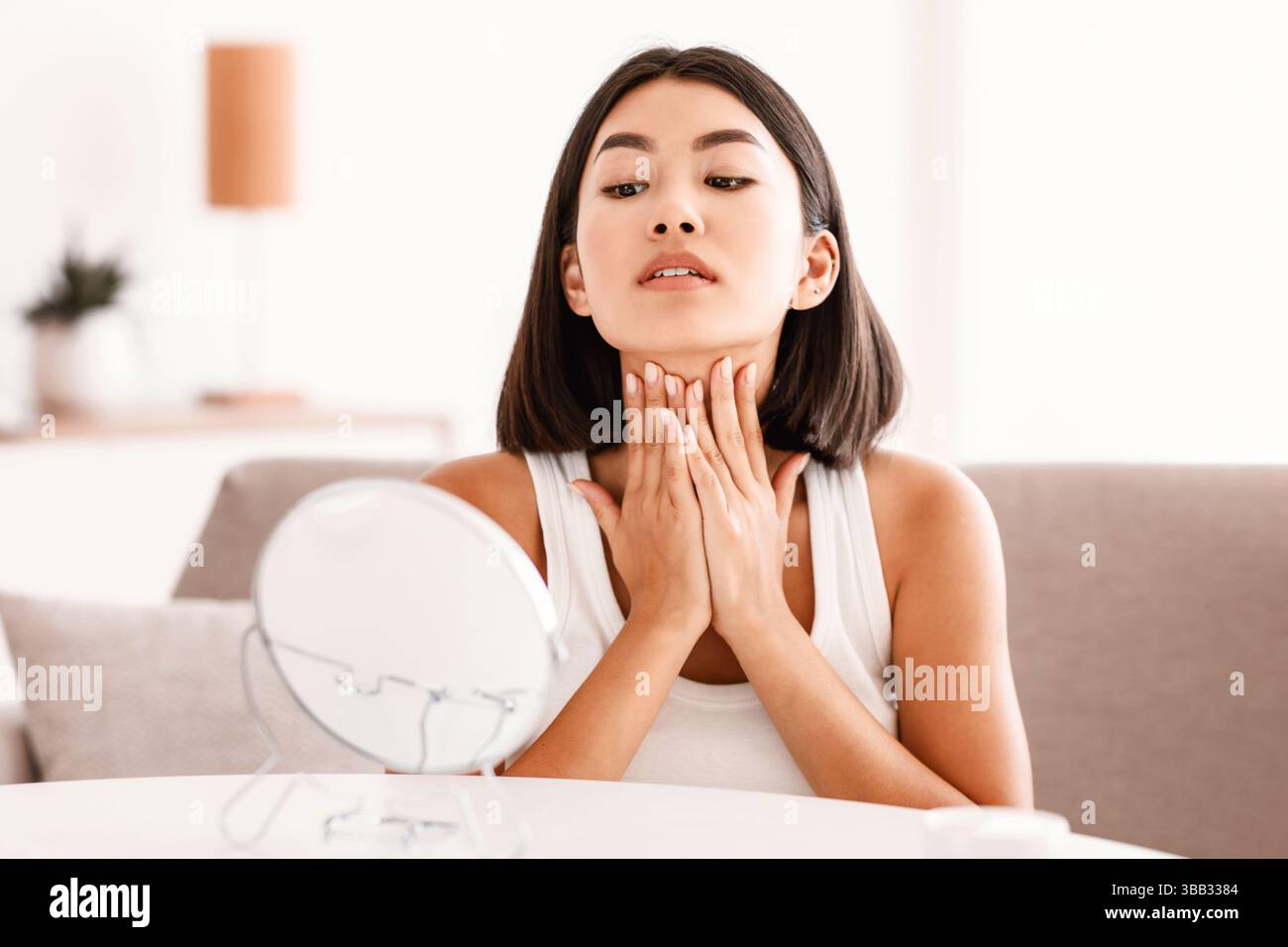 Young asian woman massaging her neck looking in the mirror Stock Photo ...