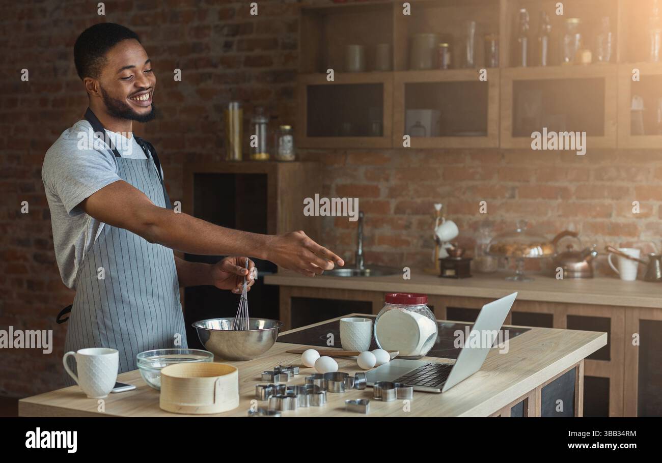 Black man baking pastry and using laptop in kitchen Stock Photo