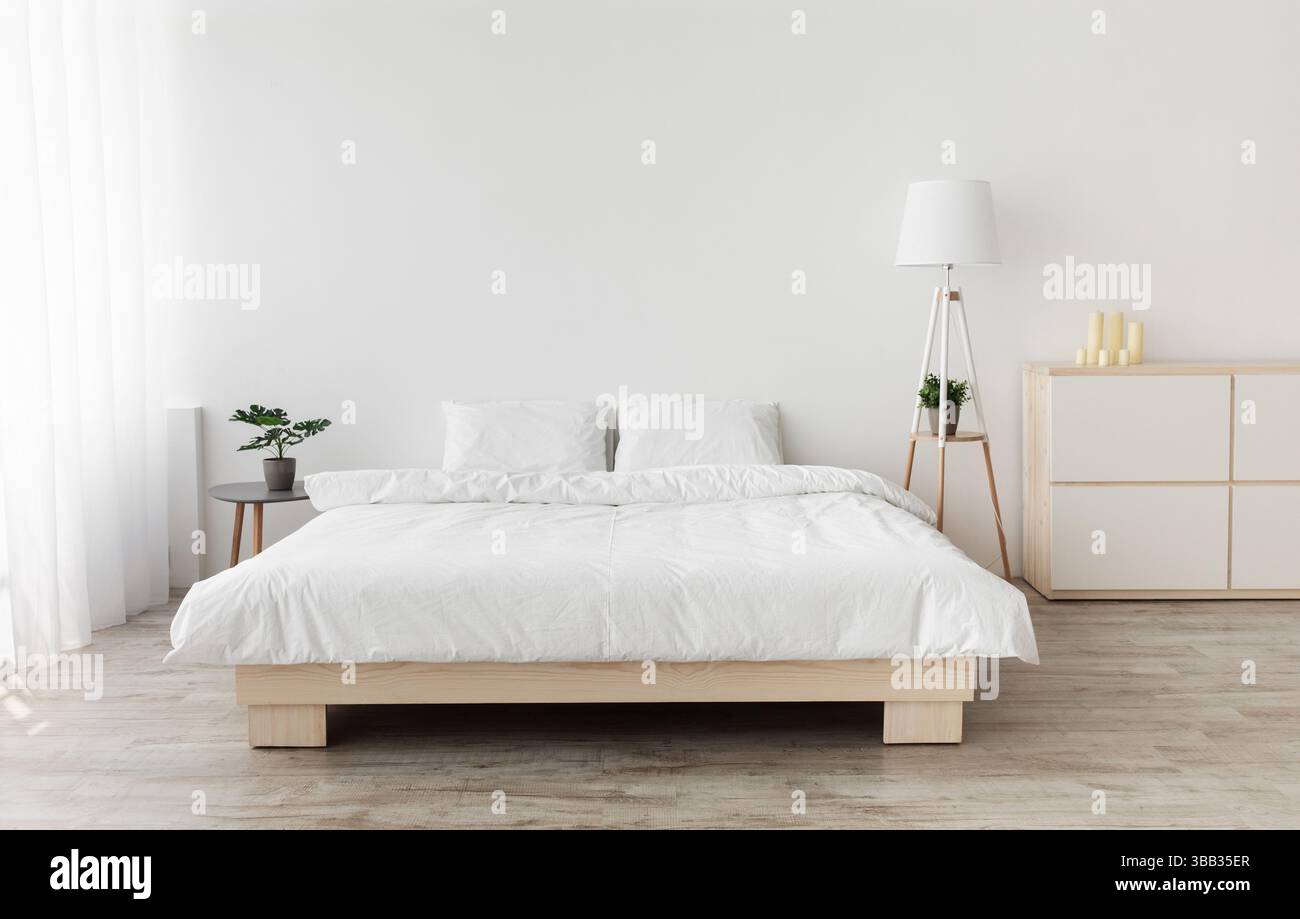 Real photo of bedroom interior in simple style. Big bed with pillows, lamp and furniture, white wall, empty space Stock Photo