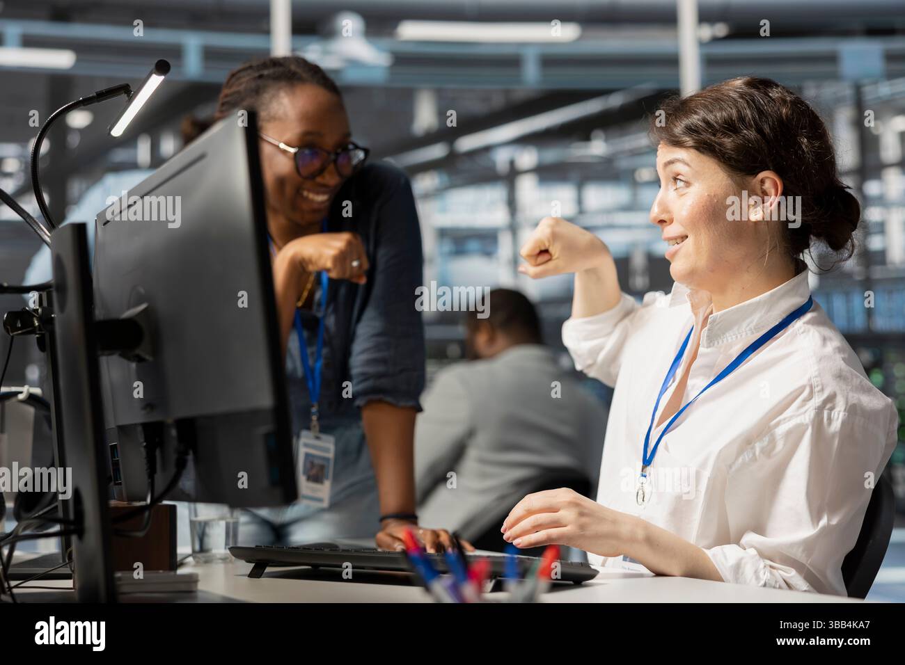 Happy server hub team leader does fist bump with worker after completing operations. Cheerful manager congratulating engineer in data center after checking report showing stable performance indicators Stock Photo
