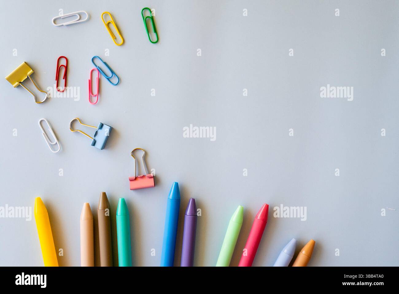 Flat lay of colorful pens paper clips and binder clips scattered on light grey background symbolizing playful creativity school supplies bright Stock Photo