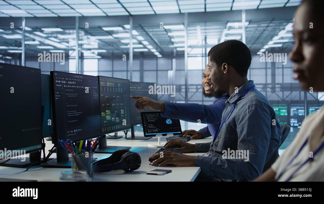 Cheerful coworkers in data center implementing AI predictive maintenance systems. Server room engineers using artificial intelligence to identify hardware failures impacting operations, camera A Stock Photo