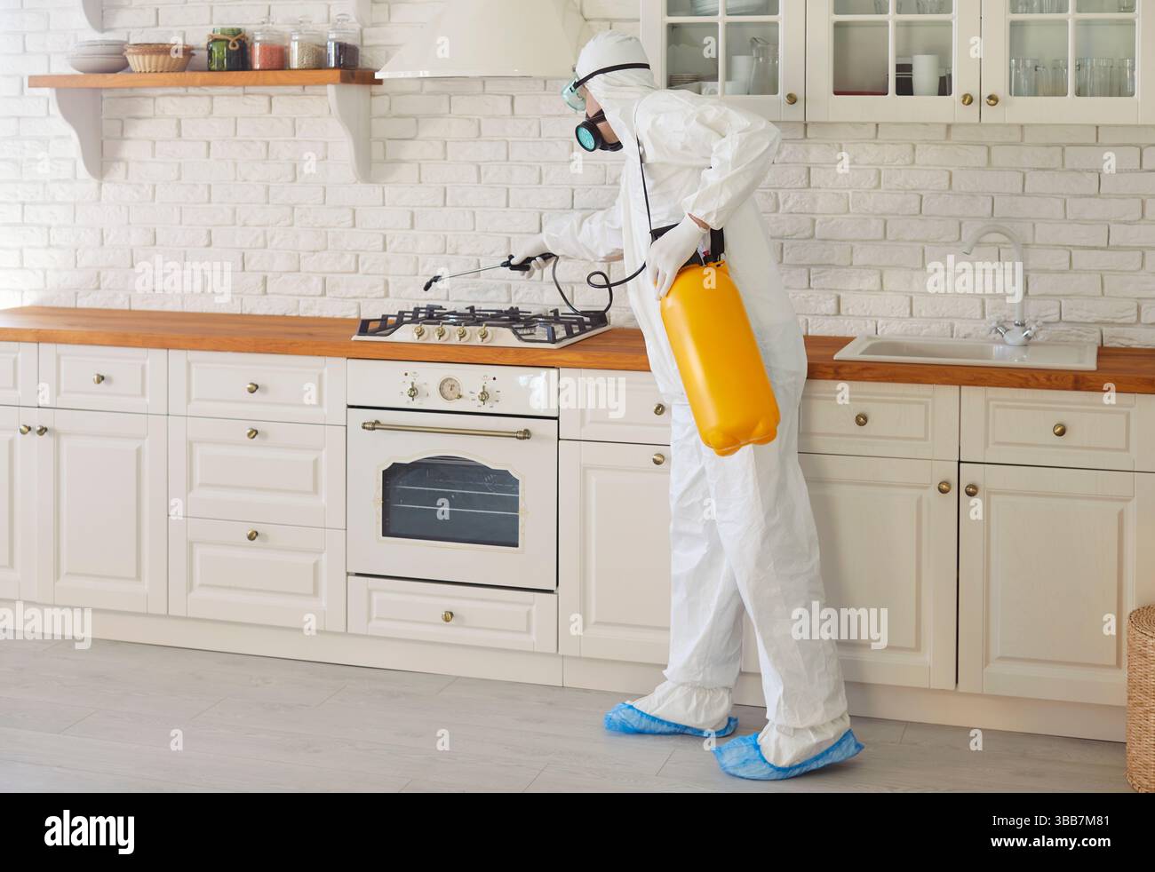 Professional worker in hazmat suit disinfecting kitchen indoor, insect killers, pandemic health risk Stock Photo
