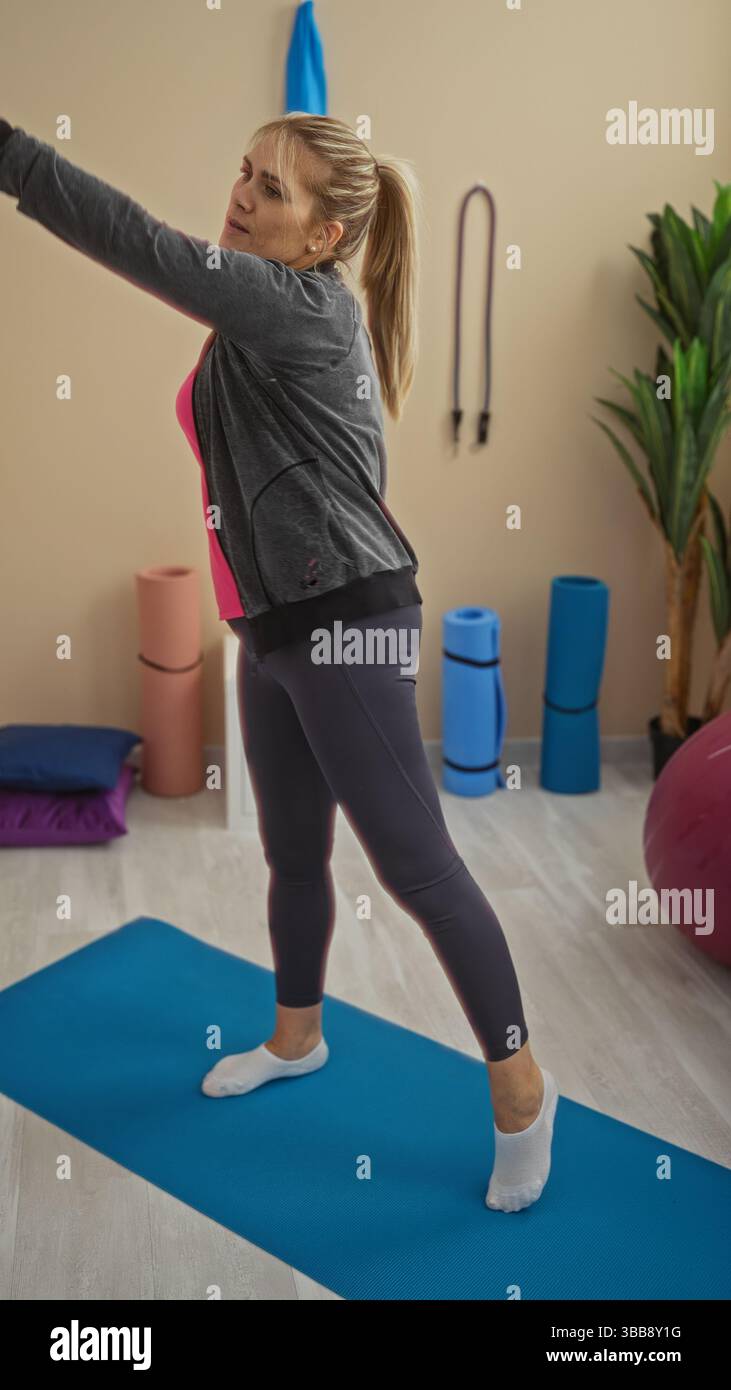 Woman exercising on mat indoors, blonde adult stretching in gym with ...