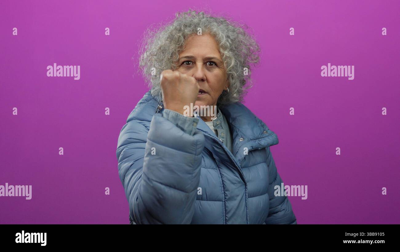 Woman with grey hair wearing blue jacket against pink background ...