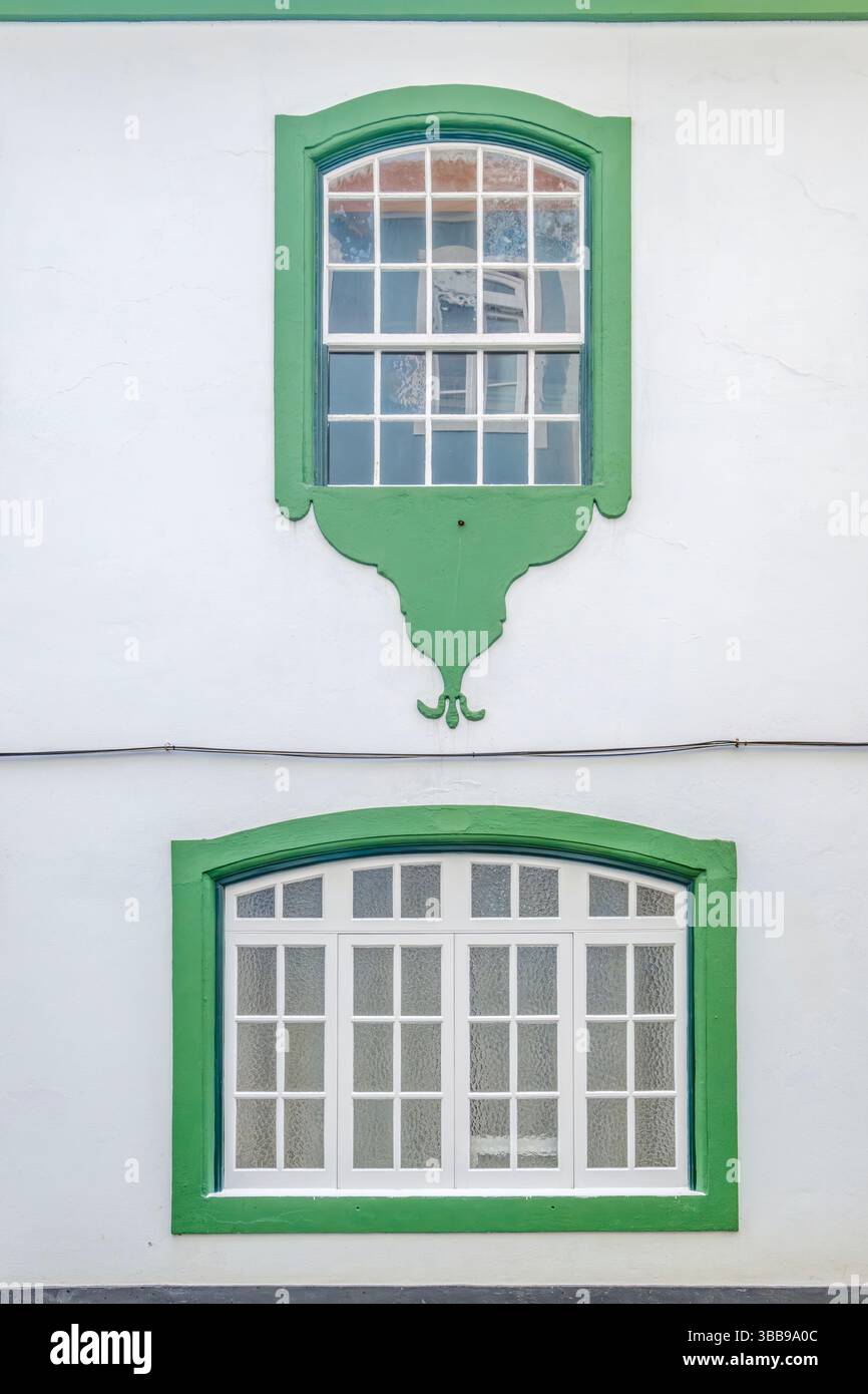 Ornate Green Windows on White Facade, Terceira. Charming close-up of two distinct windows with vibrant green frames and decorative details. The upper Stock Photo