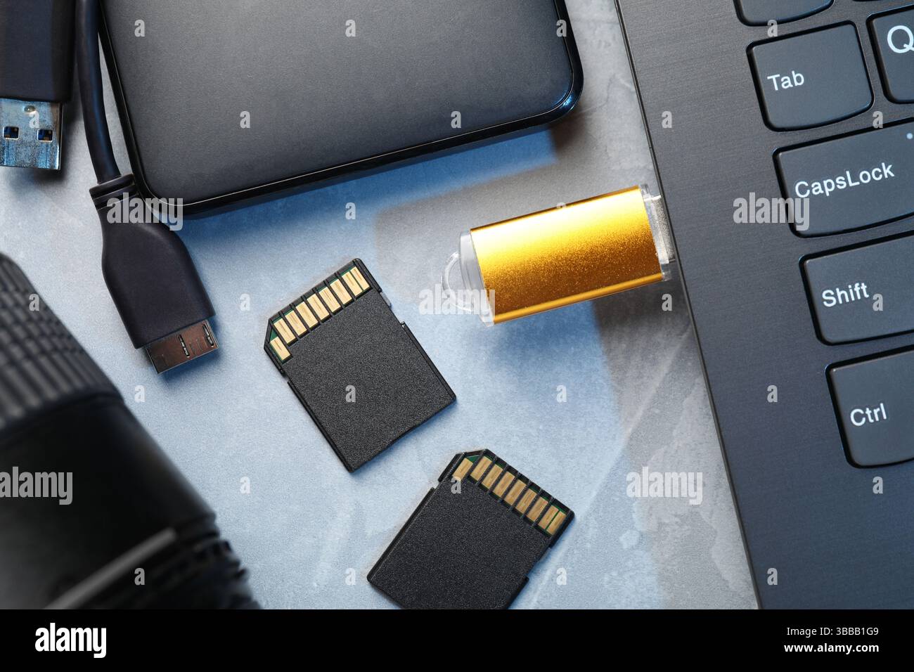 Flash drive connected to laptop, SD memory cards, external hard disk and camera lens on gray textured table, flat lay Stock Photo