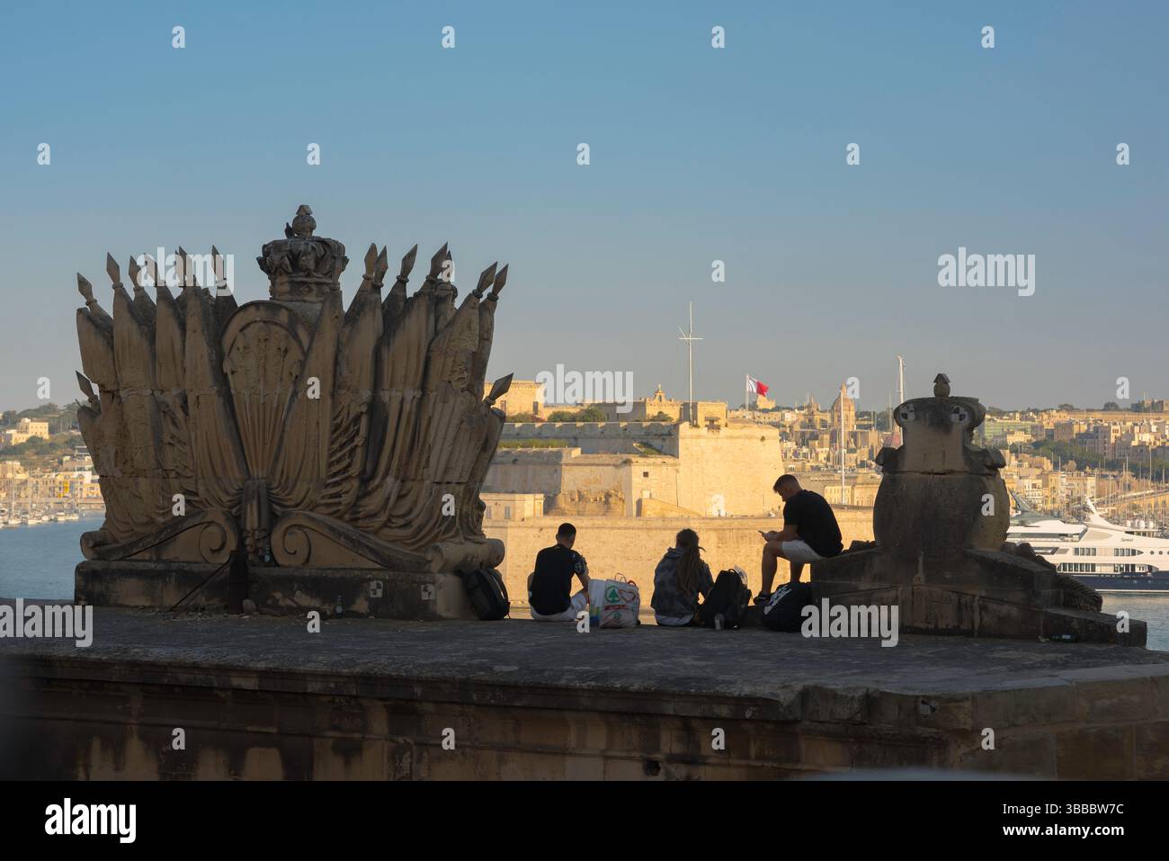 Young people travel Europe, rear view in summer of three young men looking across the Grand Harbour in the city of Valletta, Malta Stock Photo