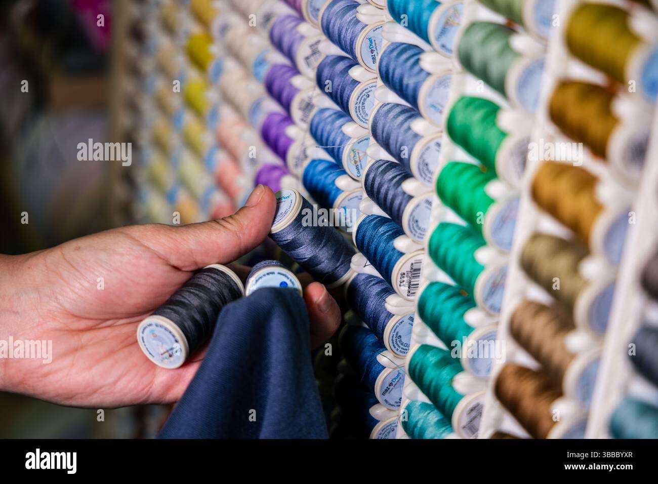 Close-up of hands comparing two spools of dark blue sewing thread to ...
