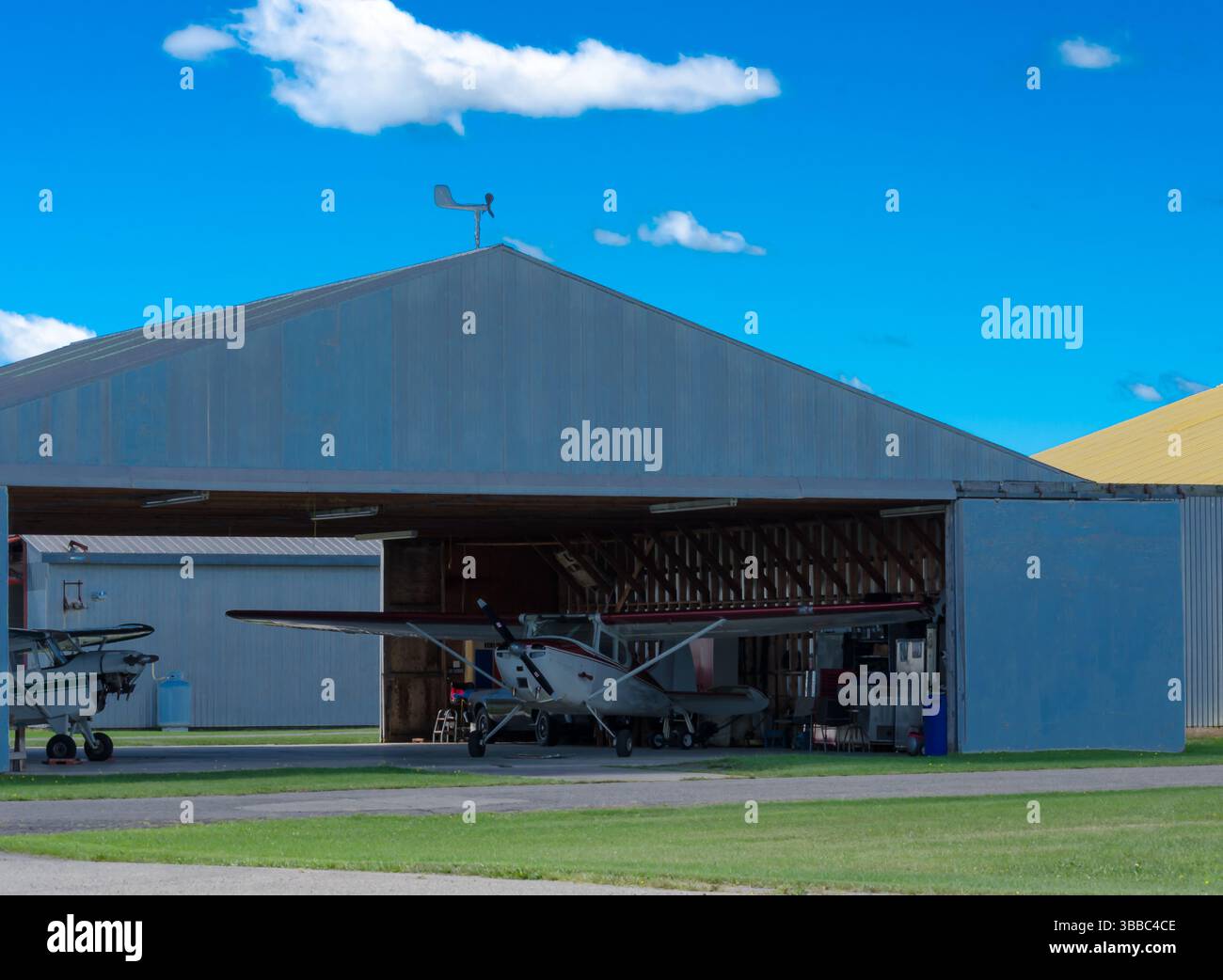 two single engine airplanes in a hangar at a rural airport under a blue ...