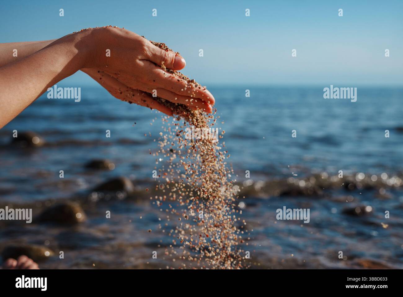 Sand falls from woman hands on sea summer background Stock Photo