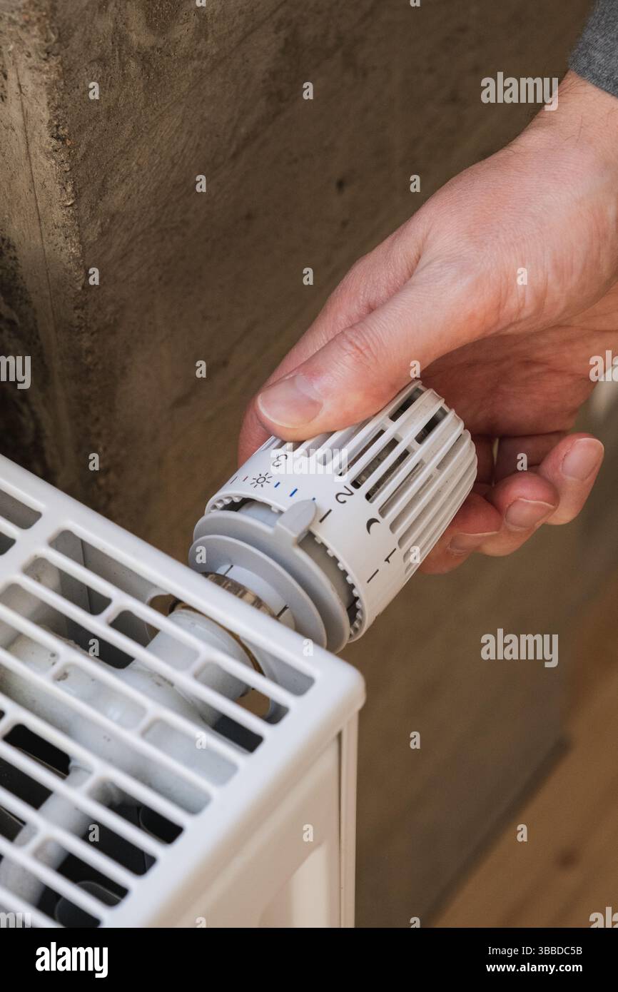 Man's hand adjusting temperature on heating radiator Stock Photo