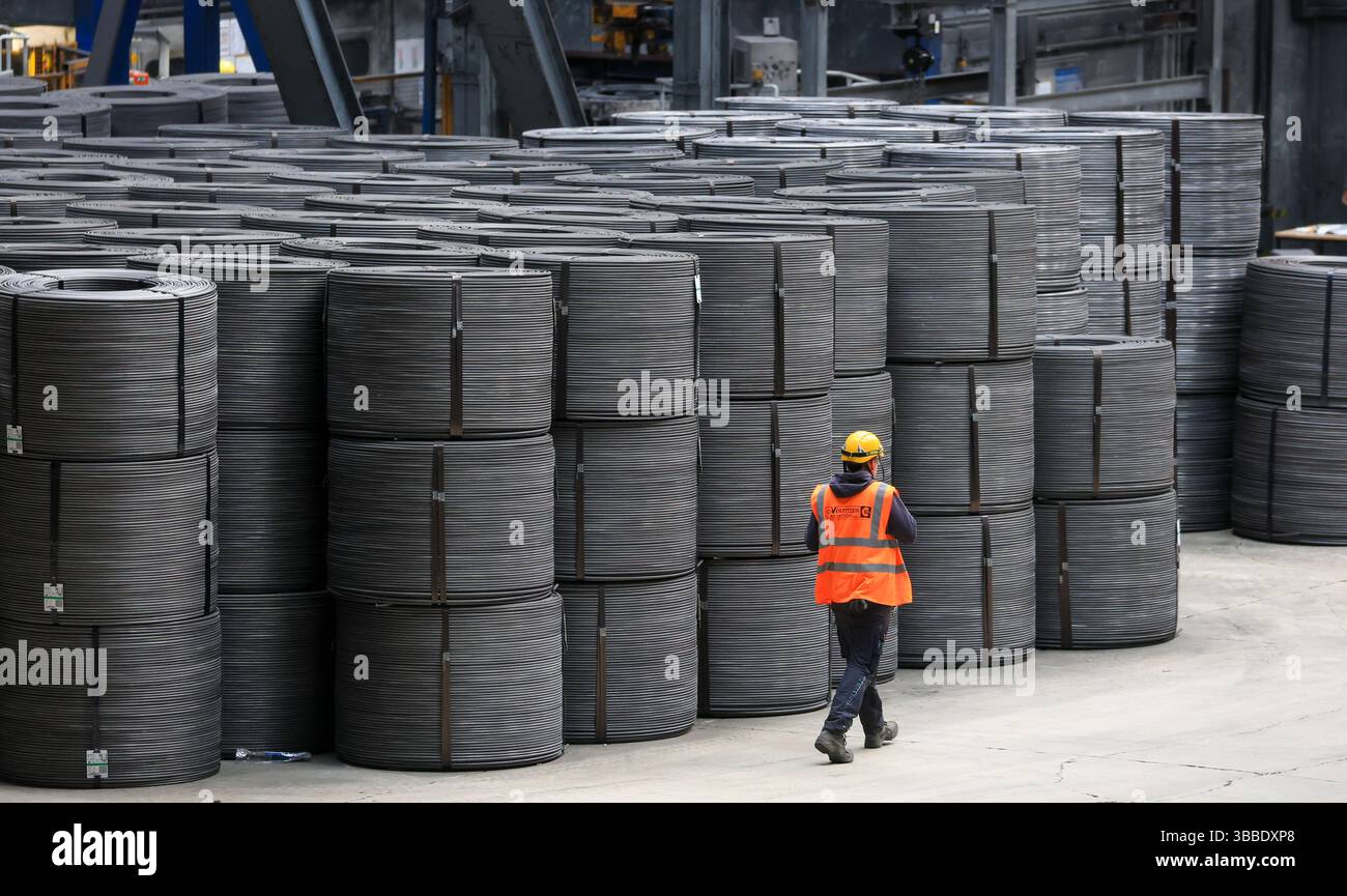 Riesa, Germany. 15th May, 2025. An employee walks past wire coils at ...