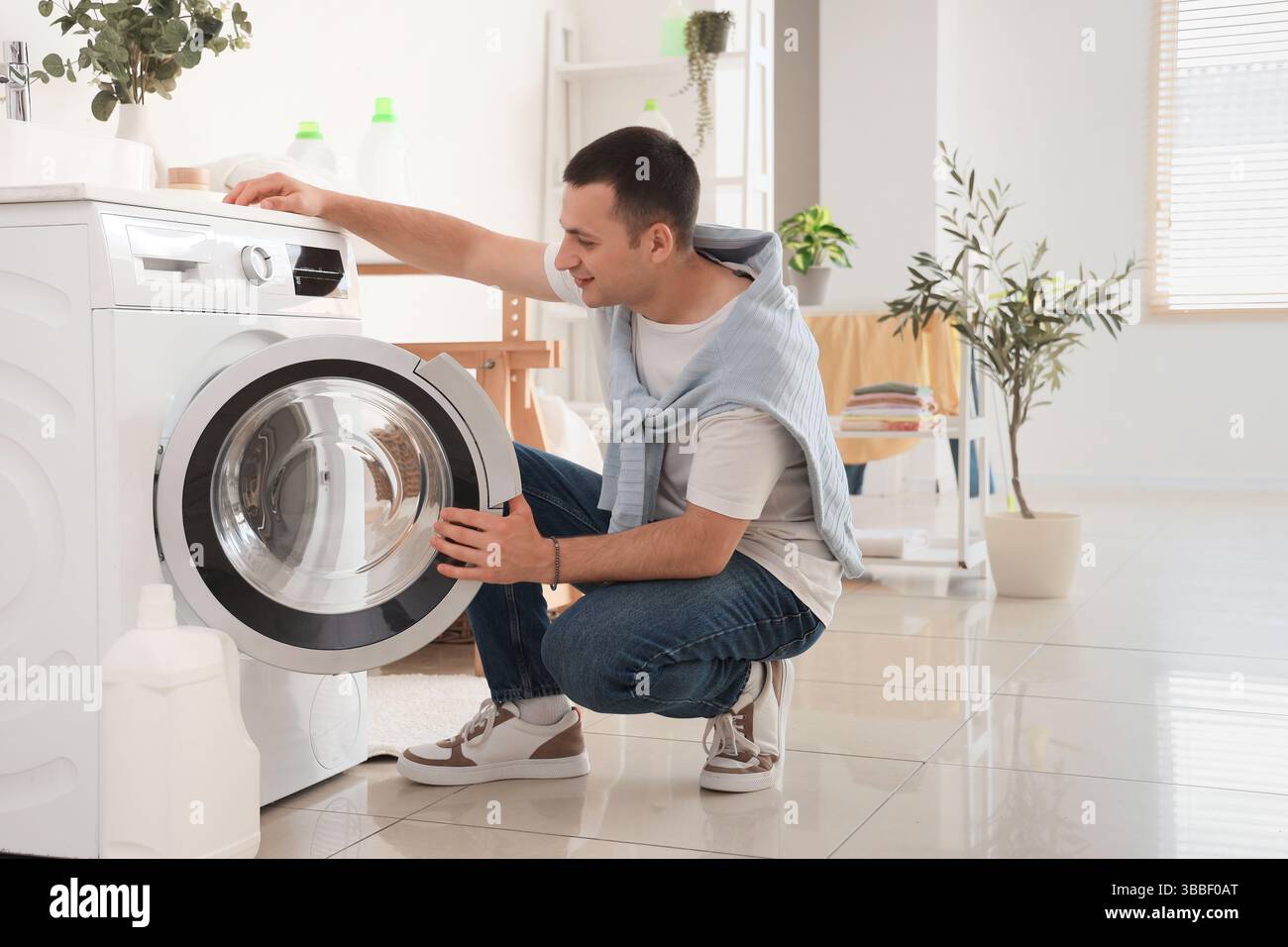 Young man using washing machine in laundry room Stock Photo