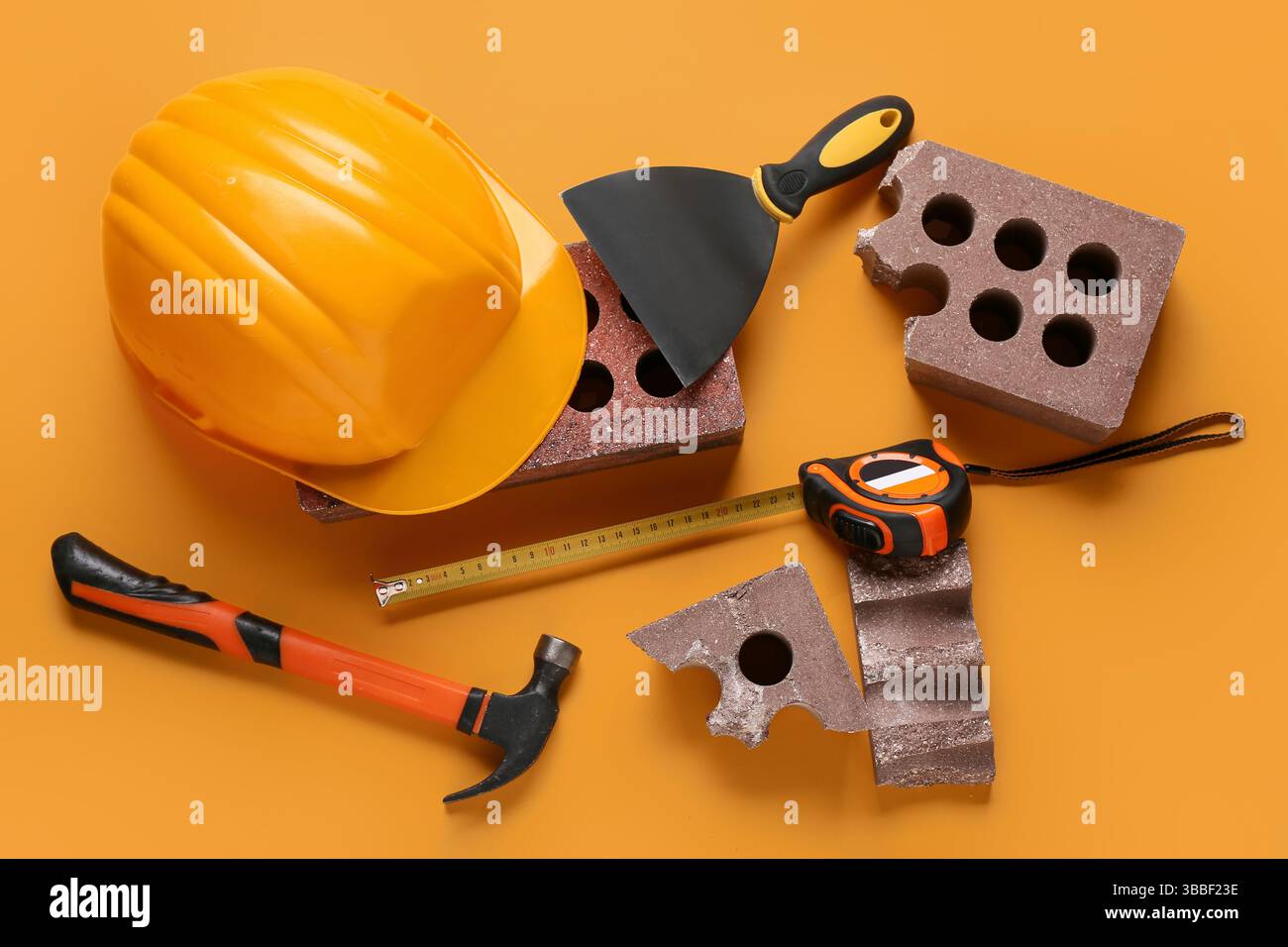 Hardhat, bricks and construction tools on orange background Stock Photo