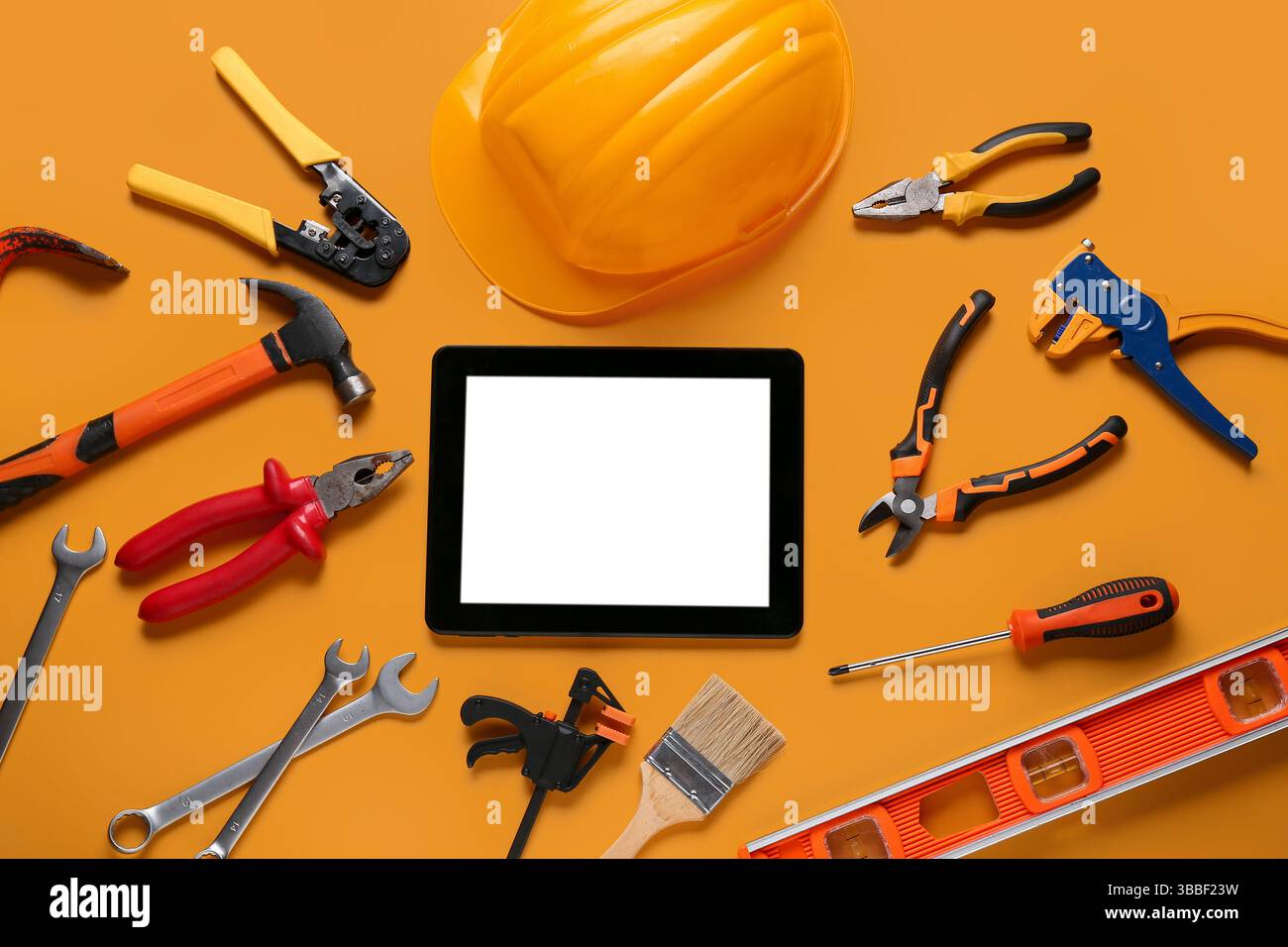 Tablet computer with blank screen, hardhat and construction tools on orange background Stock Photo