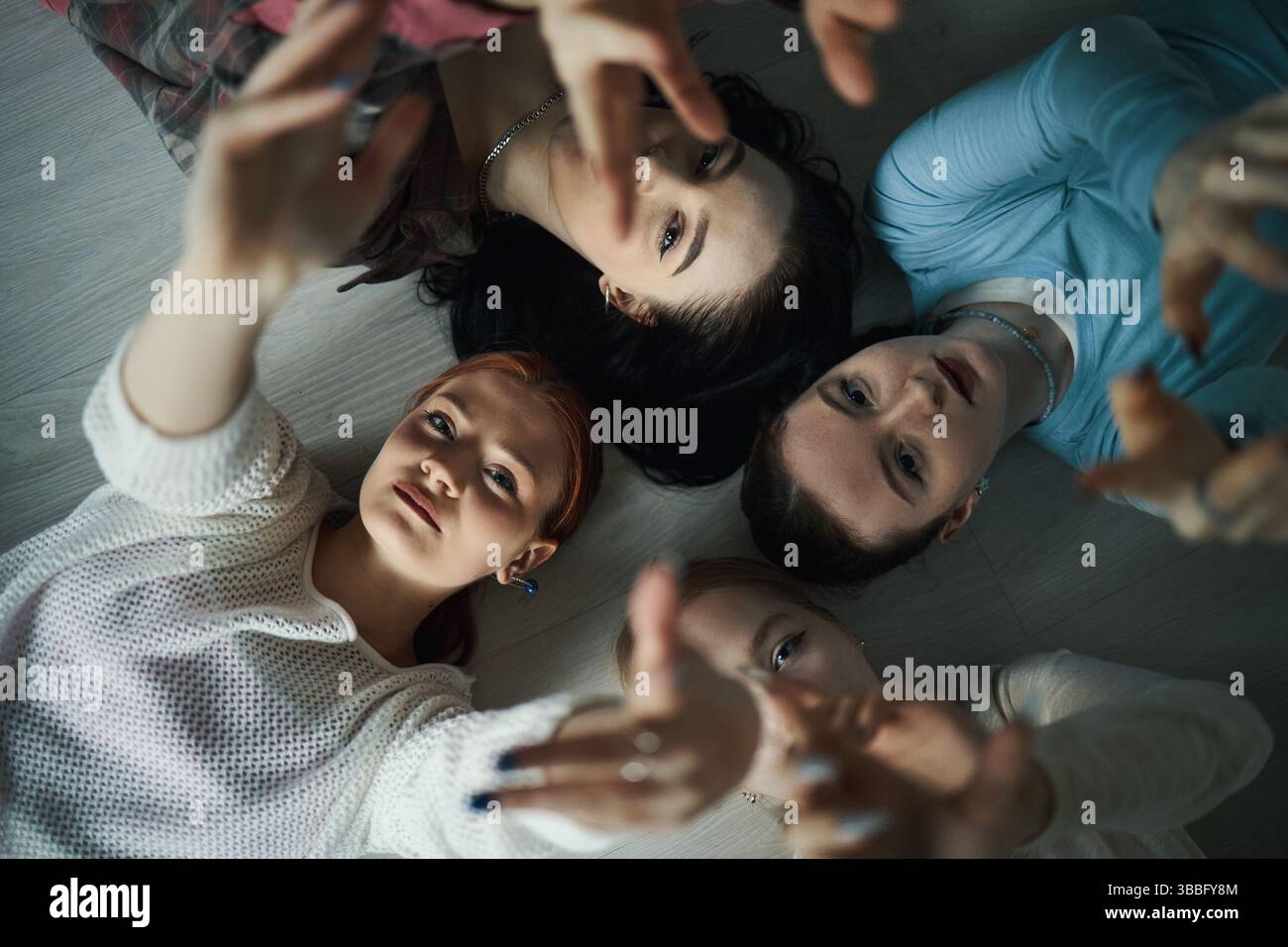 Teenagers Lying on Floor With Hands Reaching Upward Stock Photo