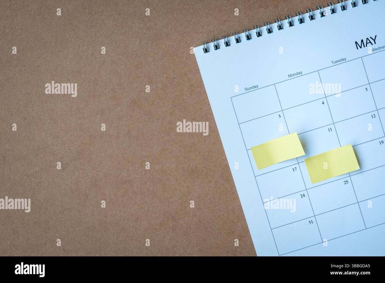 Calendar page with yellow adhesive notes. On top of brown cardboard surface, high angle view. Copy space. Stock Photo
