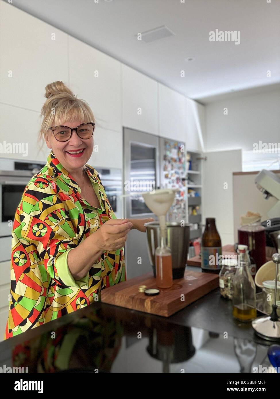 Woman in a colorful blouse bottling homemade syrup in a modern kitchen. A scene full of charm, creativity, and joyful cooking. - Smartphone Captured Stock Image