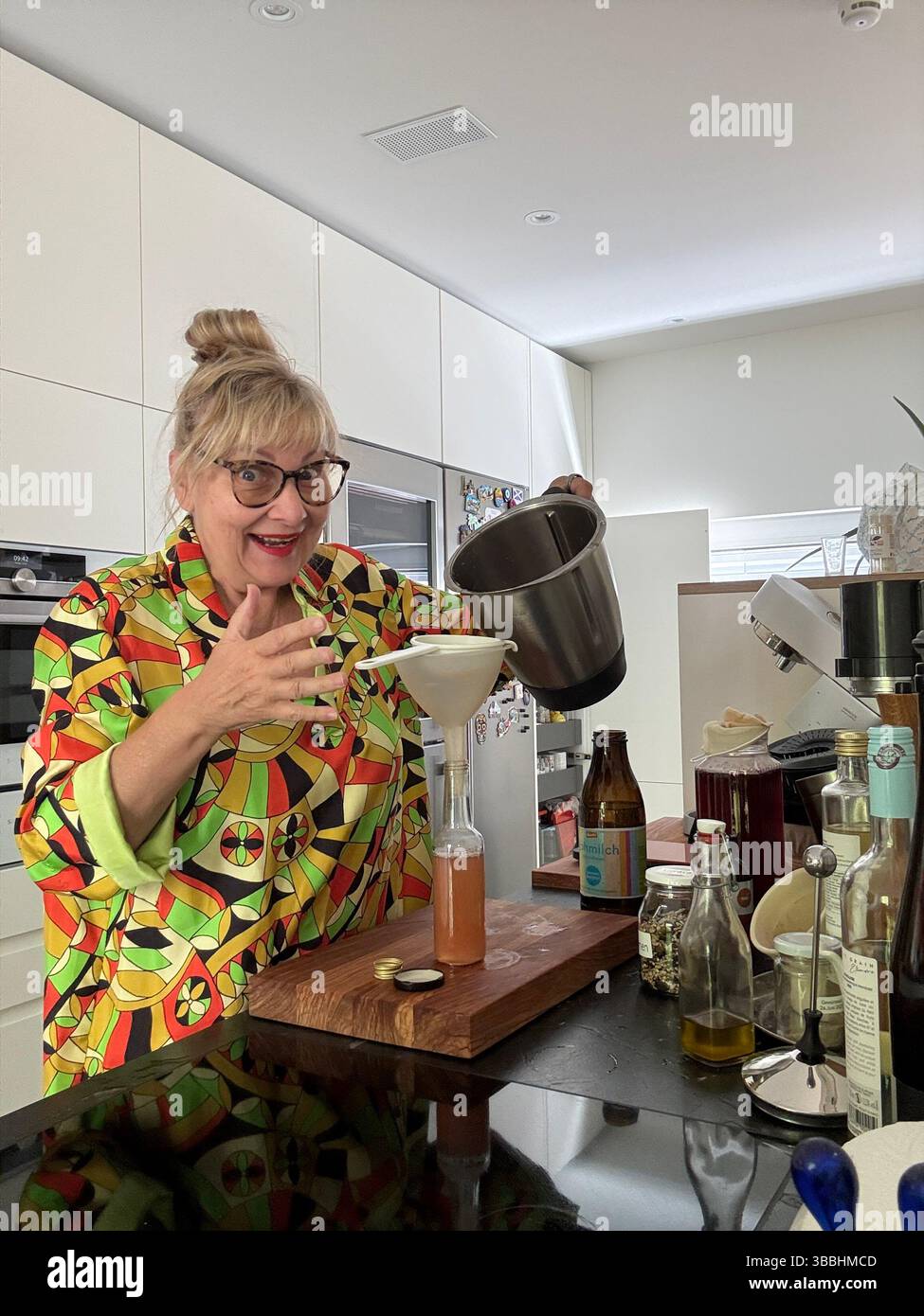 Woman in a colorful blouse bottling homemade syrup in a modern kitchen. A scene full of charm, creativity, and joyful cooking. - Smartphone Captured Stock Image