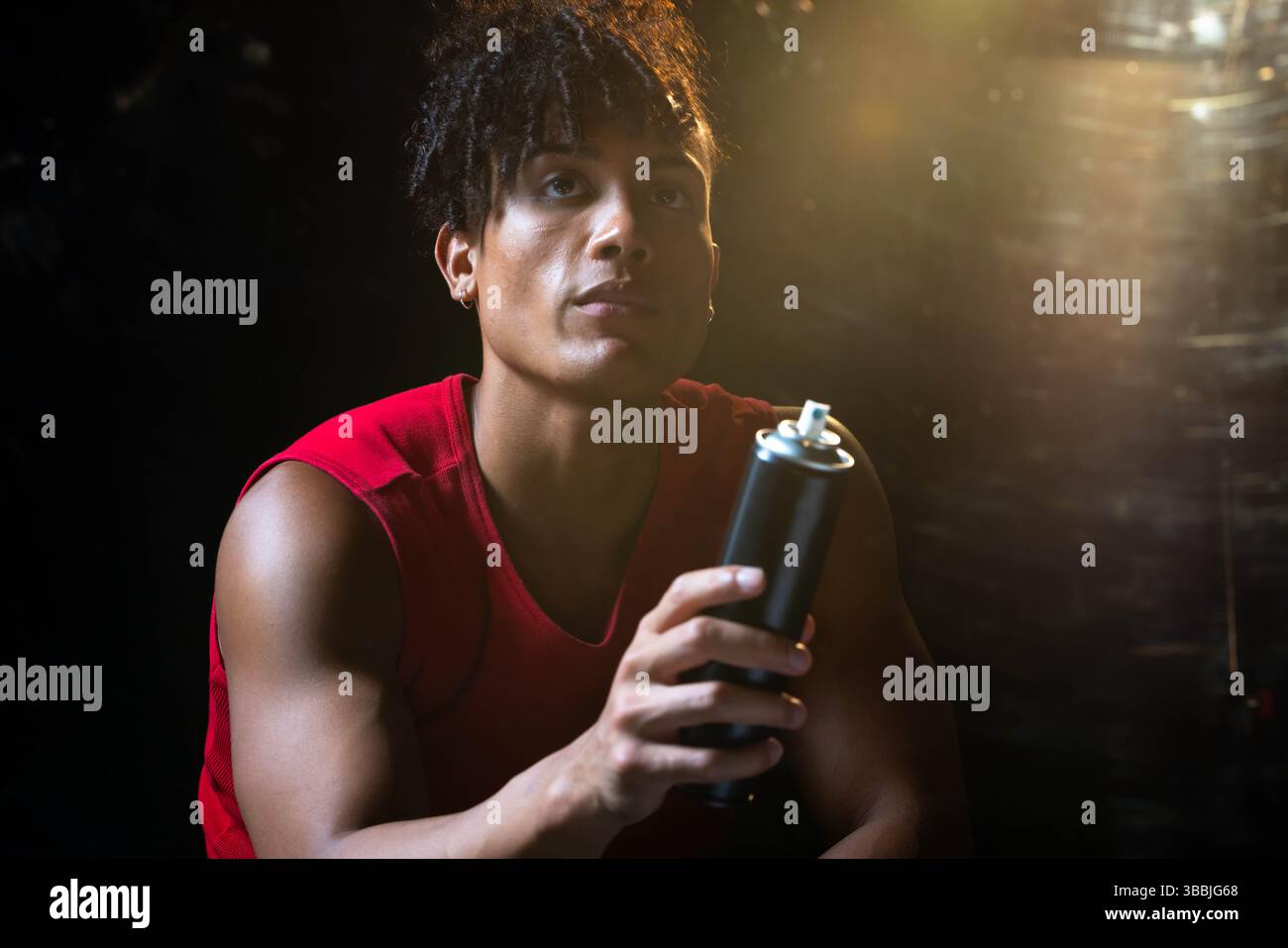 Holding African American man in red shirt spraying wall in studio, with black spray paint can Stock Photo