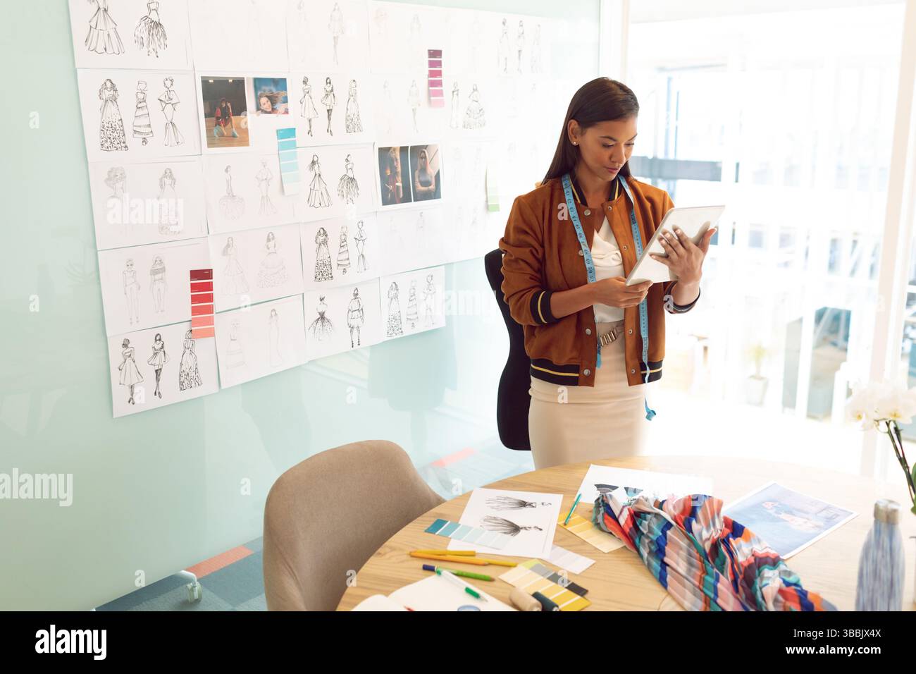 Woman reviewing sketches in fashion studio, with tablet, measuring tape ...