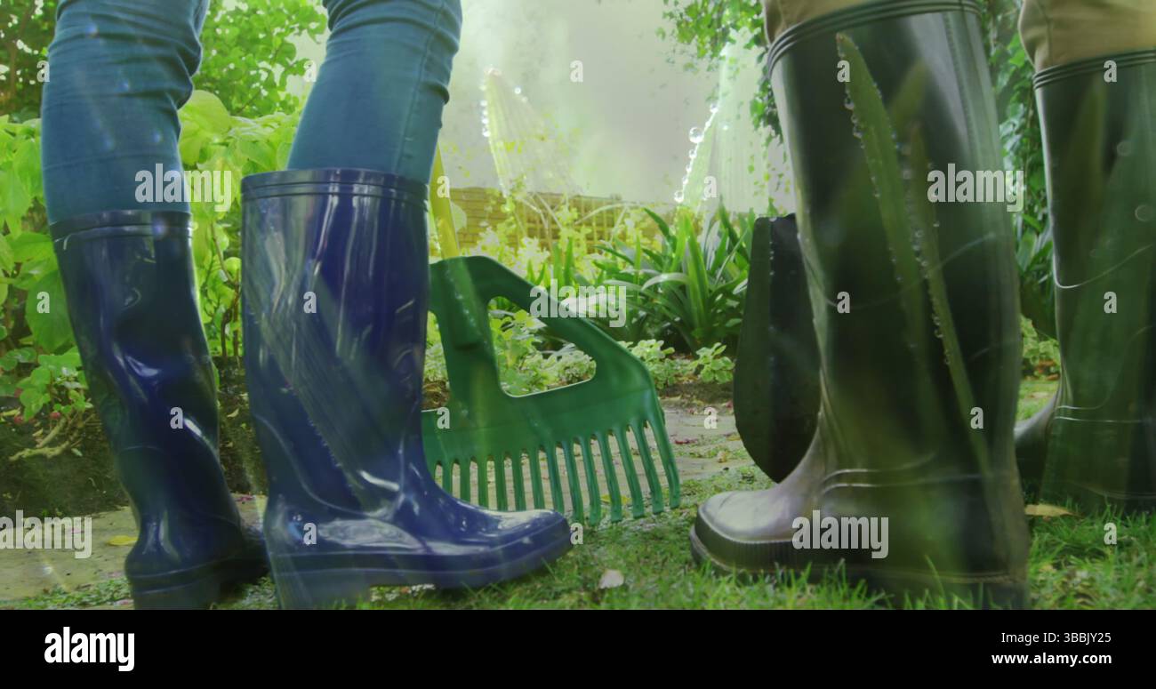Image of grass over legs of two people wearing rubber boots working in garden Stock Photo