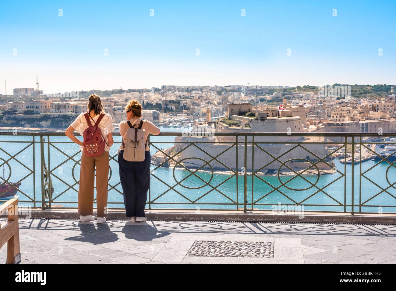 Women travel friends, rear view of two female travellers looking across the Grand Harbour in the city of Valletta, Malta Stock Photo