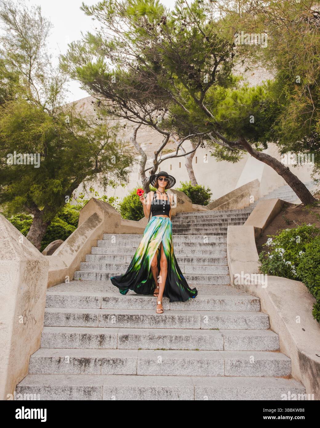 Fashionable woman is walking down the stairs  towards camera in beautiful old stone city town Calvi in island Corsica, France. Stock Photo
