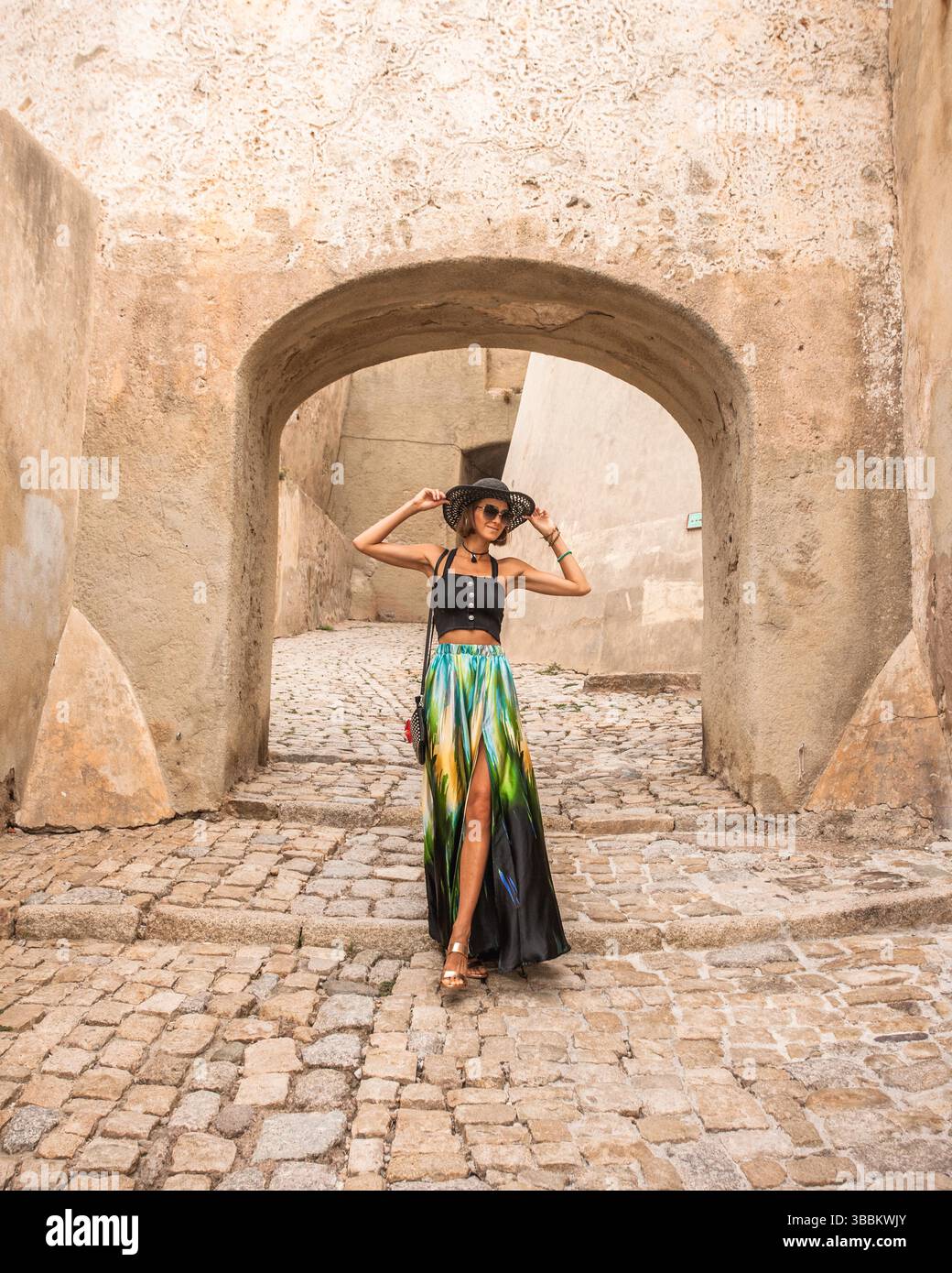 Portrait of fashionable woman walking  trough beautiful old stone city town Calvi in island Corsica, France. Model wears elegant  feminine outfit. Stock Photo