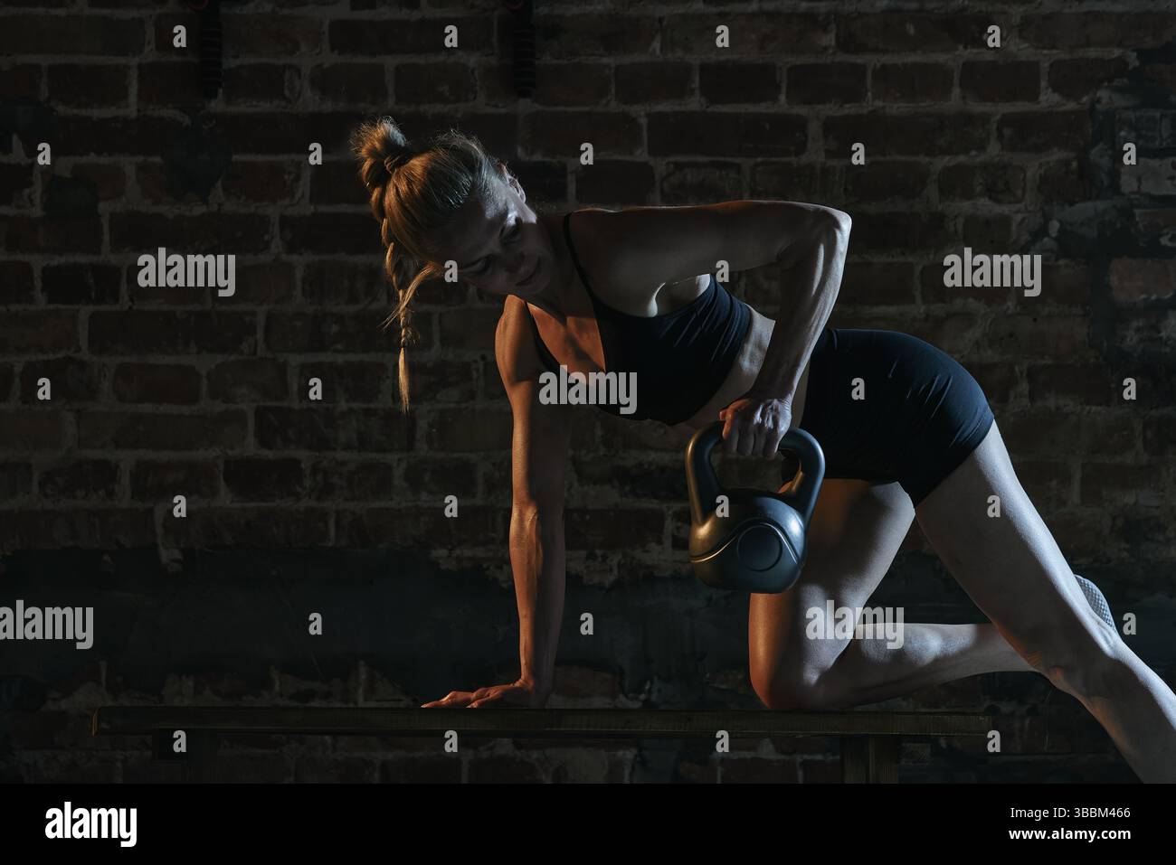 Strong woman in gym lifting kettlebell during bench workout with ...