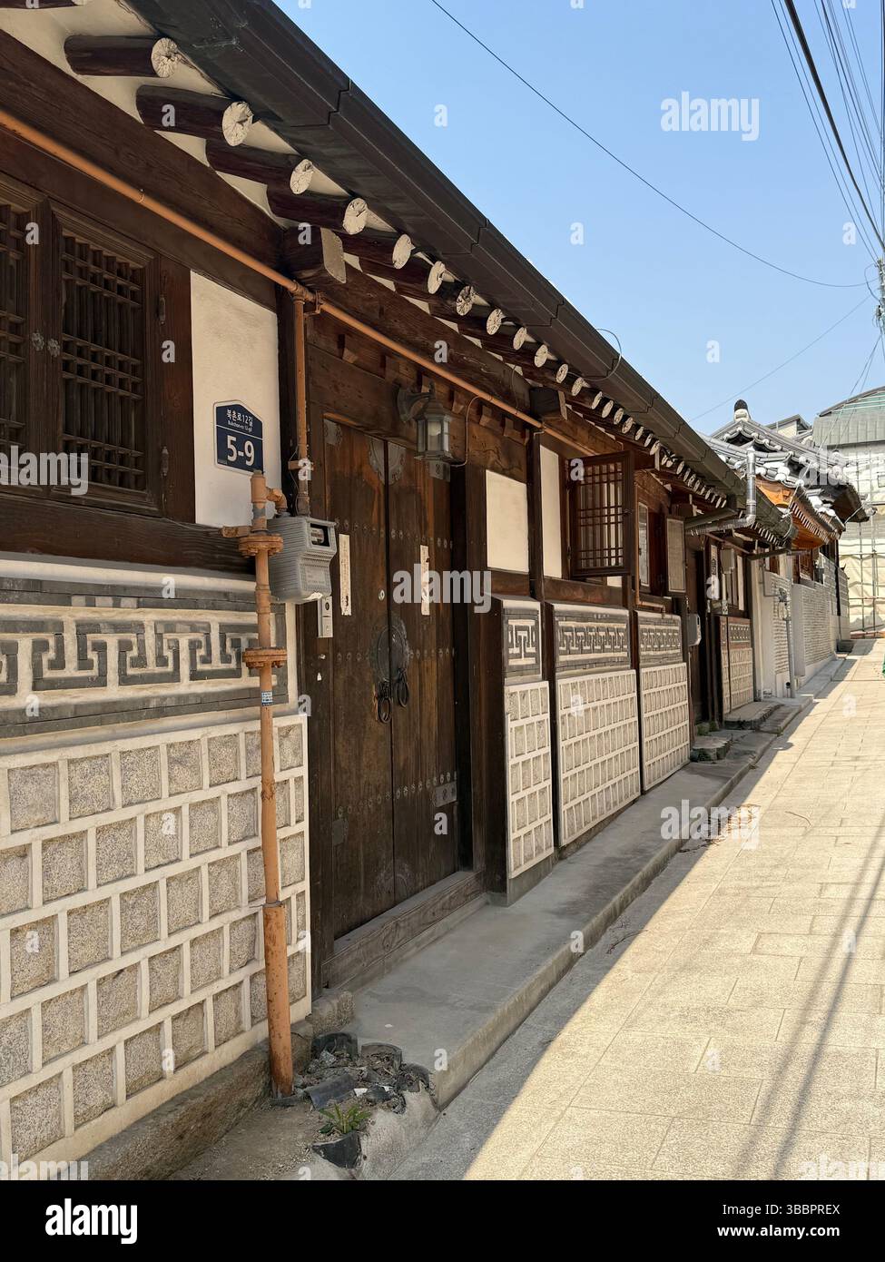 Traditional Korean Hanok homes with wooden doors and tiled walls line a quiet street in a historic district under clear skies. - Smartphone Captured Stock Image