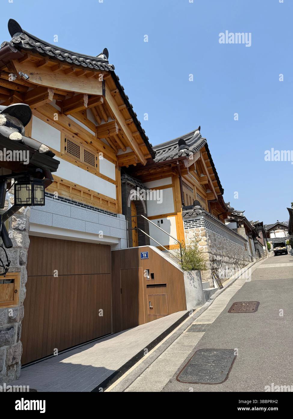Traditional Hanok design meets modern architecture on a quiet street in South Korea, under a cloudless blue sky - Smartphone Captured Stock Image