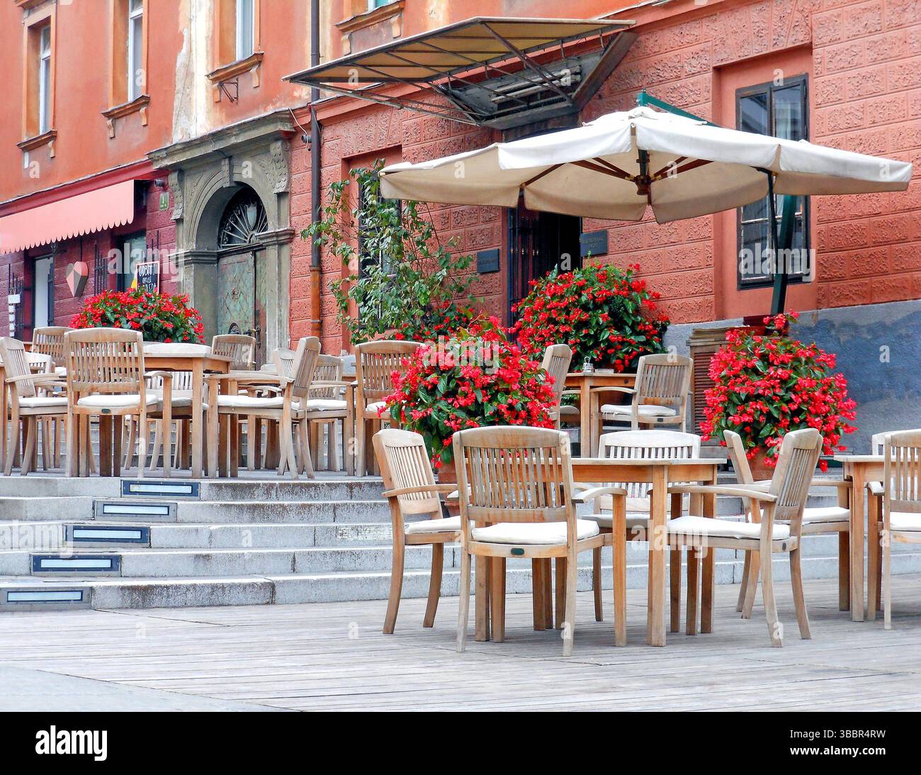 Ljubljana Slovenia. July 26 2012. Empty café terrace with wooden furniture and vibrant flowers along colorful building façade Stock Photo