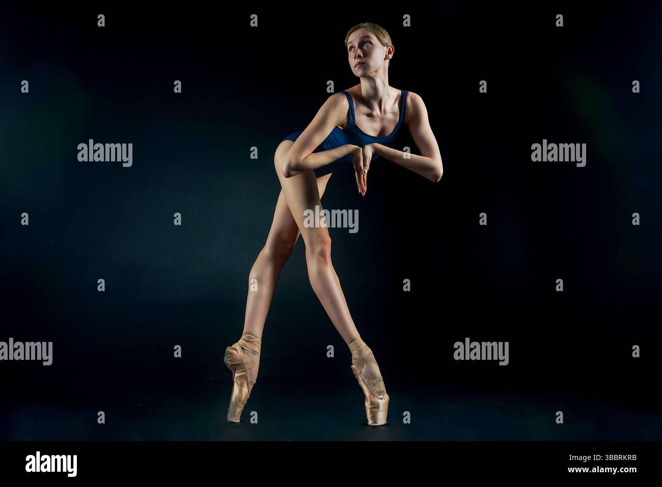 a ballerina on a dark background stands on pointe shoes demonstrating ...