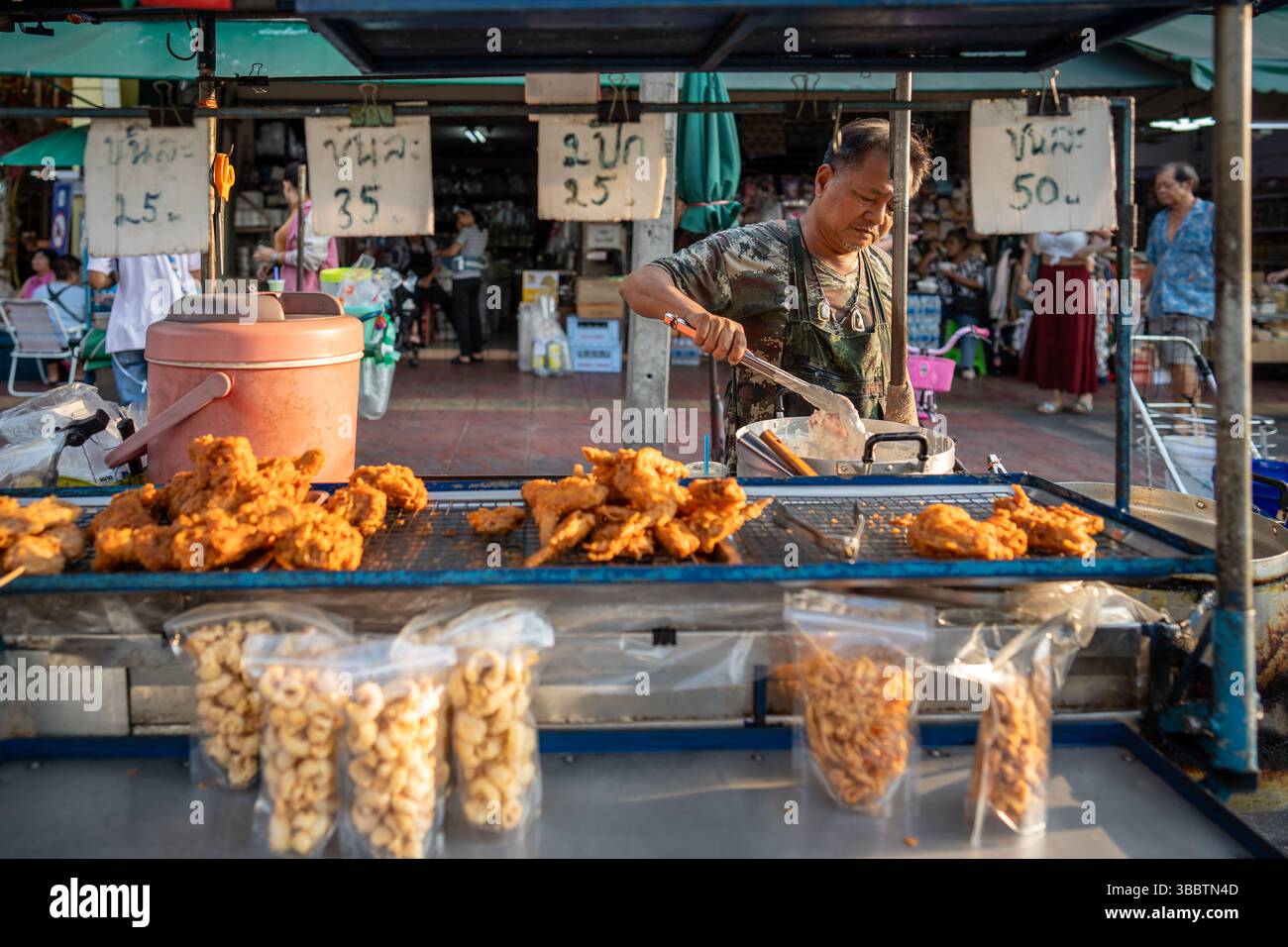 Man sells fried battered seafood at street food stall with price tags on finished dishes outdoors Stock Photo