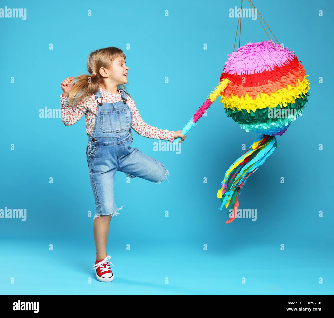 Happy girl breaking bright pinata with stick on light blue background ...