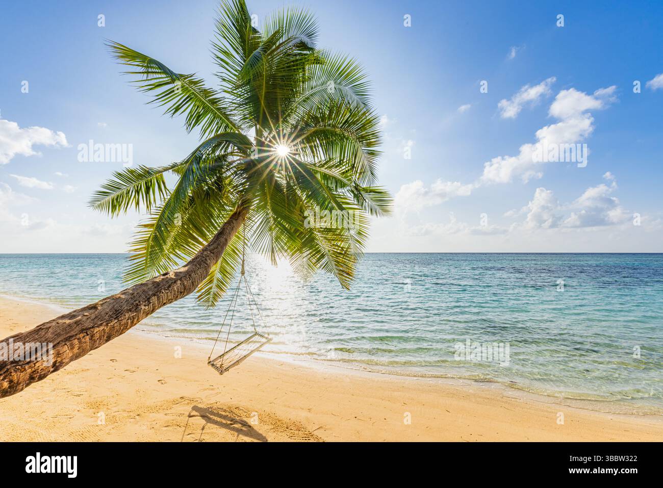 Palm tree swing on tropical beach at sunrise with golden rays, beautiful tranquil landscape full of serenity, peaceful summer morning by the sea Stock Photo