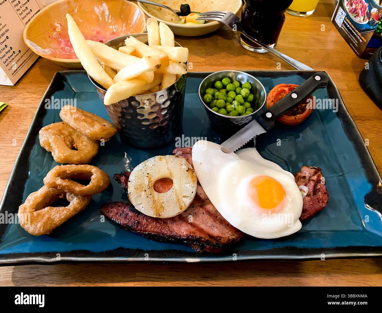 A meal of gammon steak with pineapple, fried egg, onion rings, chips and peas in a restaurant as part of a meal out - Smartphone Captured Stock Image