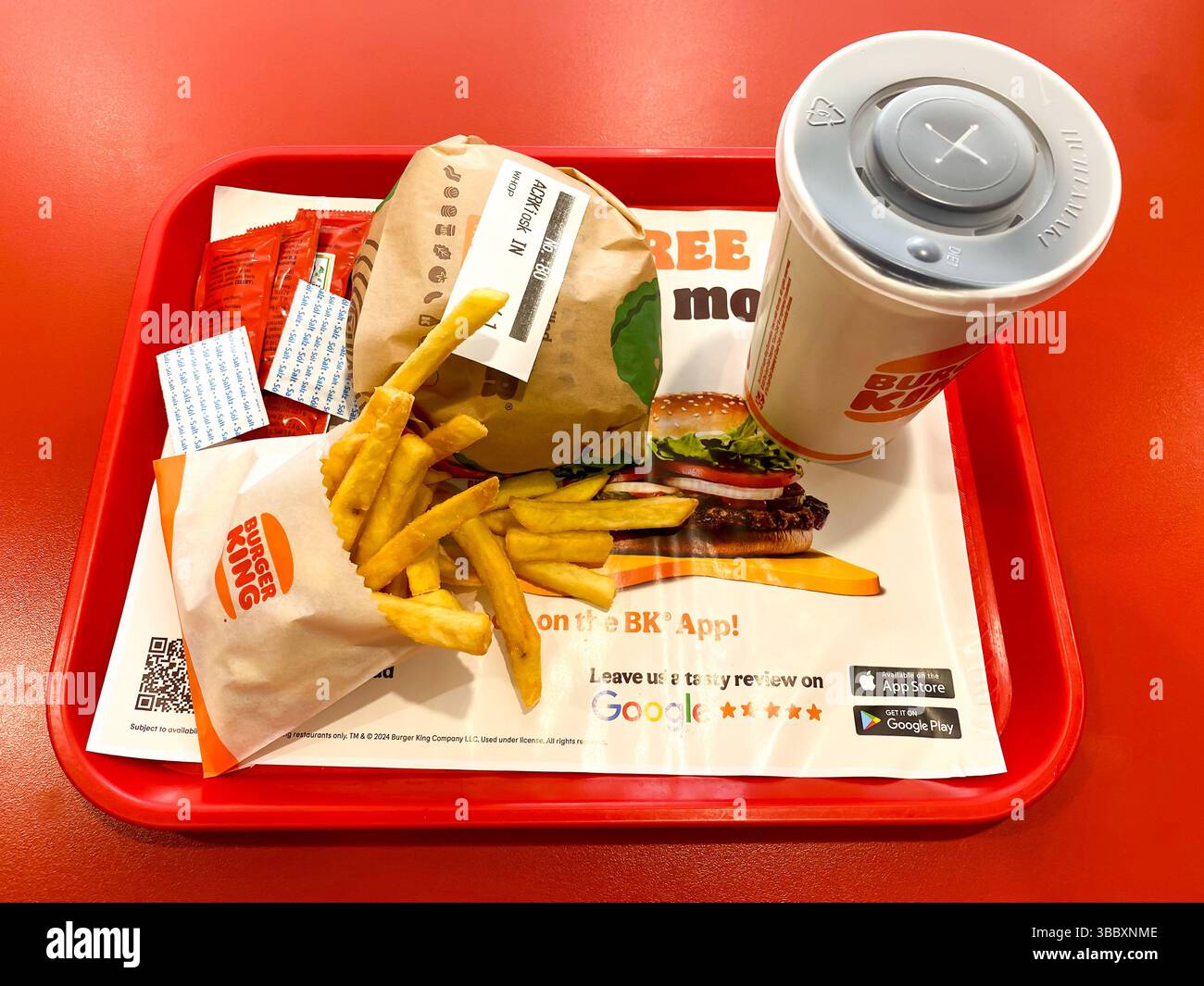 A whopper meal purchased at a Burger King fast food restaurant. A whopper burger and a cup of soda are seen on a tray on a table. - Smartphone Captured Stock Image