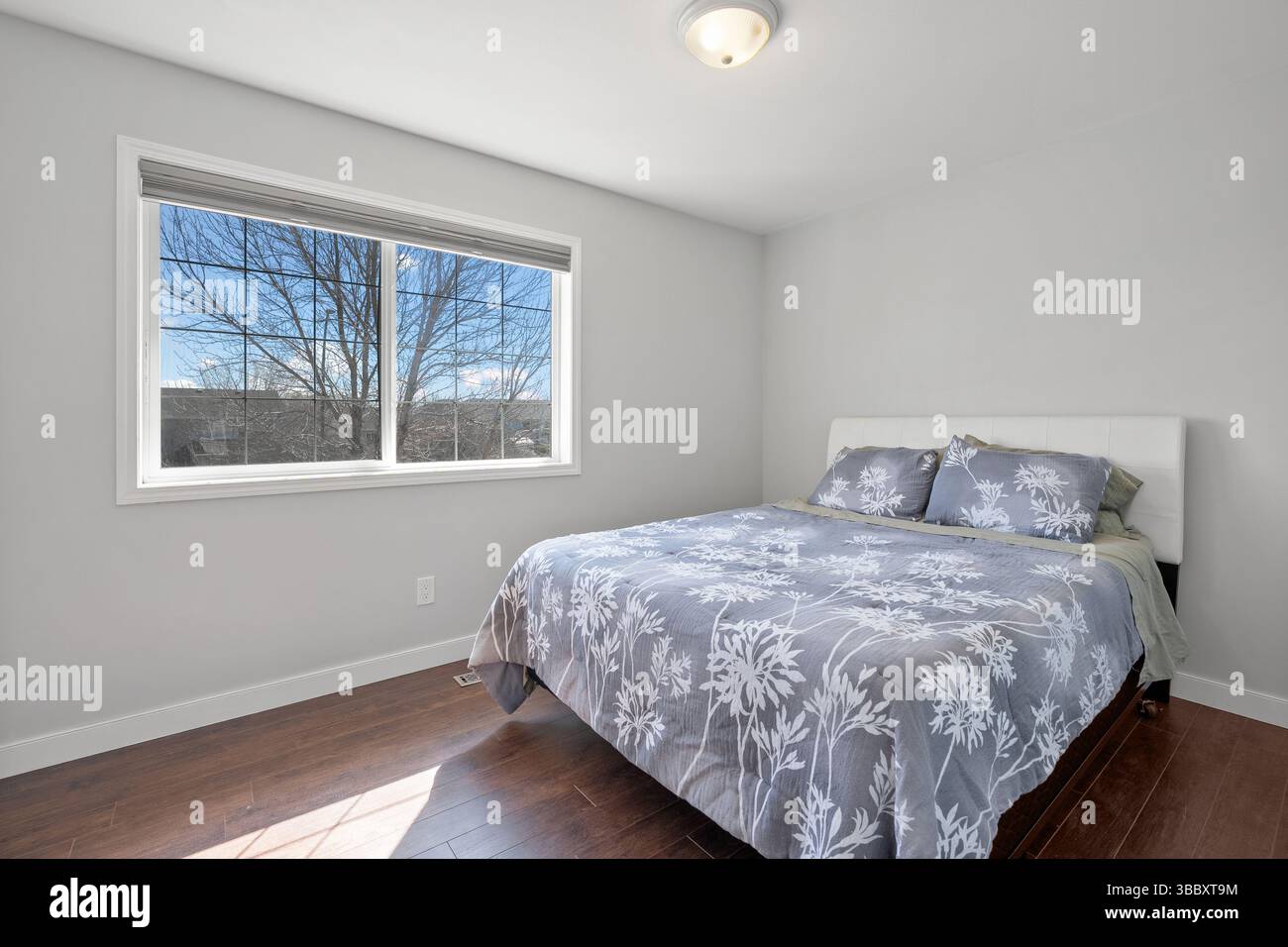 Bedroom with a large bed and a window. The window is open, letting in a cool breeze. The bed is covered in a floral patterned comforter. The room is c Stock Photo