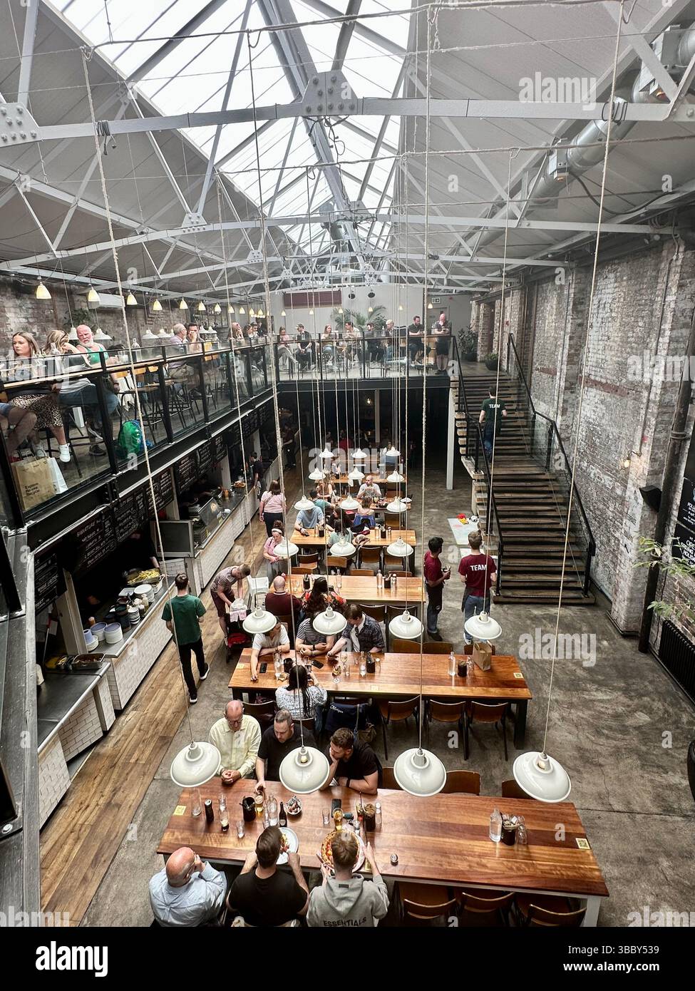 View from mezzanine of Duke Street Market, Liverpool, showing industrial interior, metal frame, brick walls, tables, and people on both floors. - Smartphone Captured Stock Image