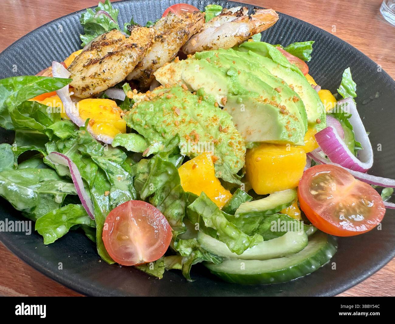 Fresh avocado, mango, and prawn salad with lettuce, cherry tomatoes, and red onions in a grey bowl. Healthy and colorful meal. - Smartphone Captured Stock Image